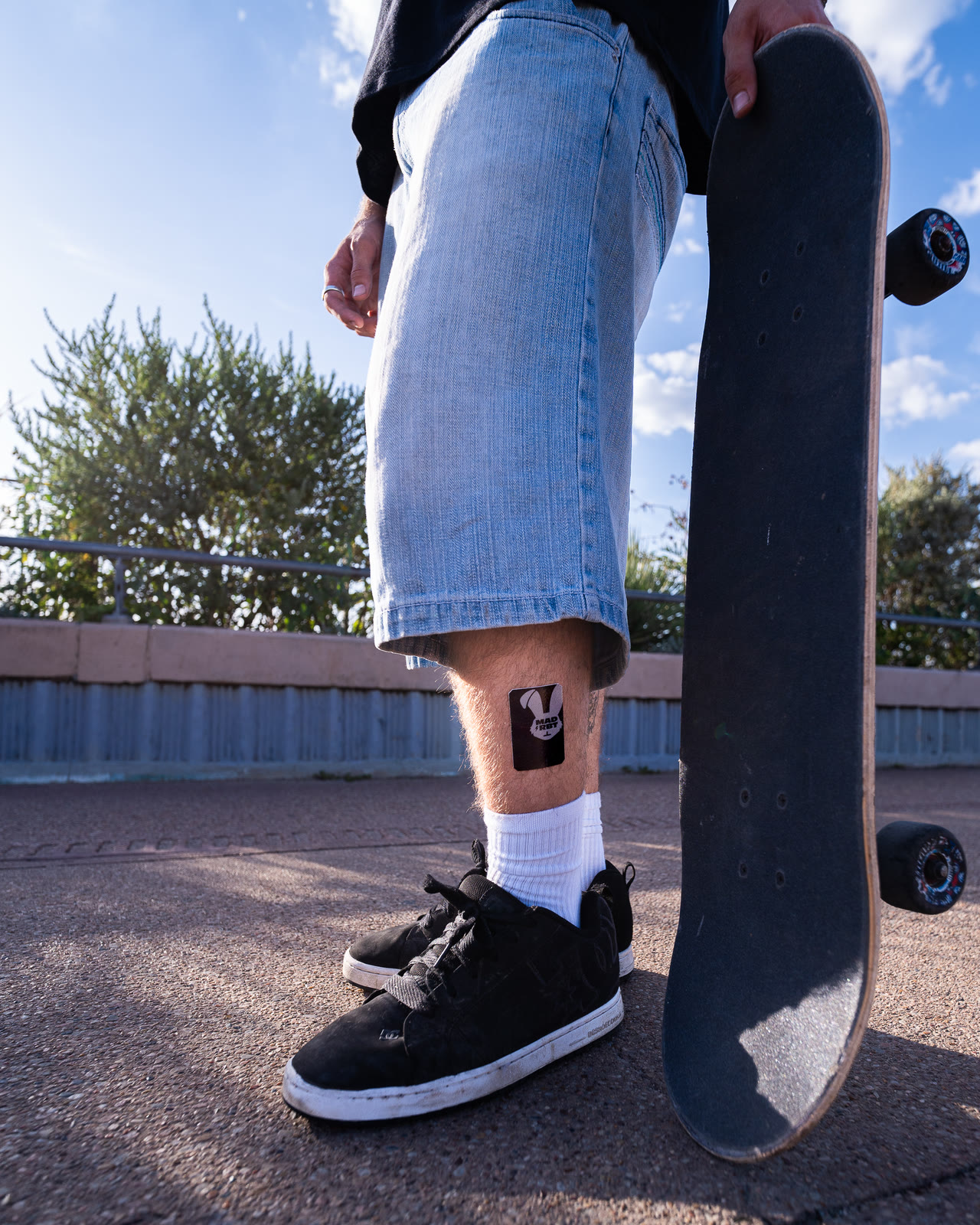 Skater standing with a board, Mad Rbt patch on the calf