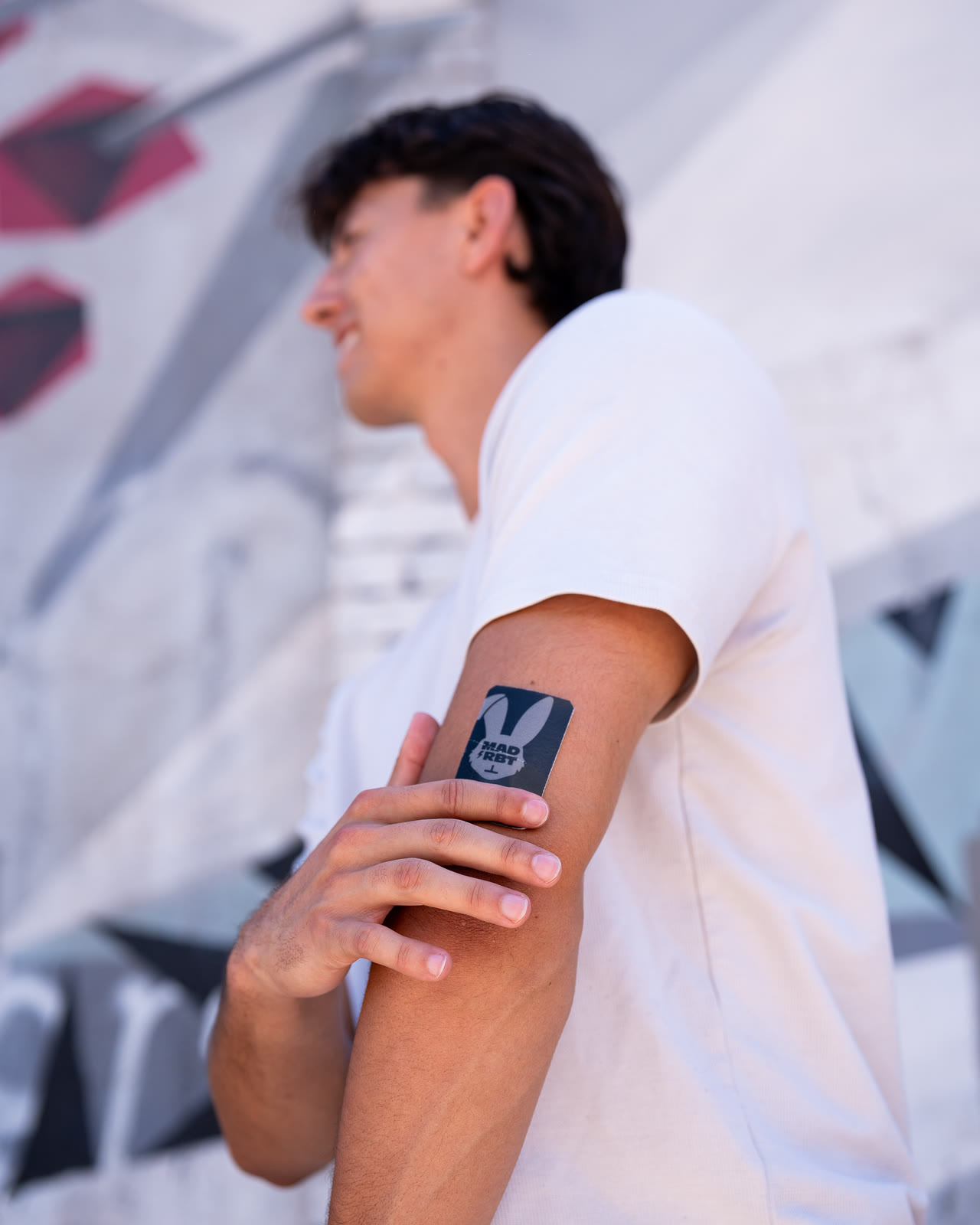 Man with a Mad Rbt patch on his upper arm in front of a mural